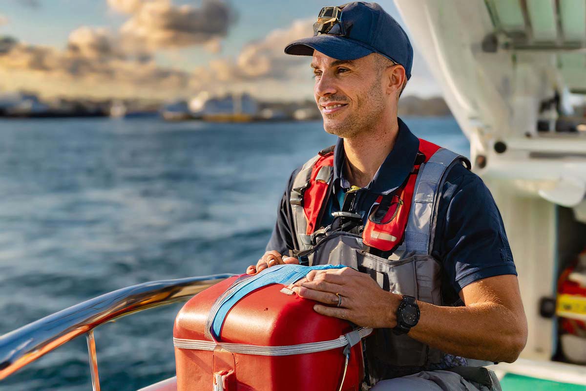 A person standing on the bow of a boat holding a first aid kit, about to deliver some essential marine first aid