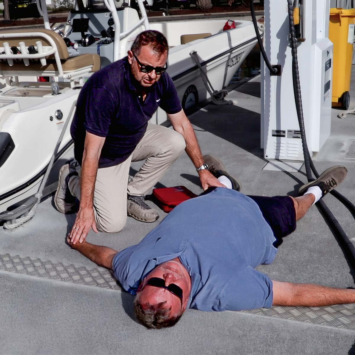 An Advanced Marine First Aid Responder attending to a prone casualty on the wharf of a marina beside a boat