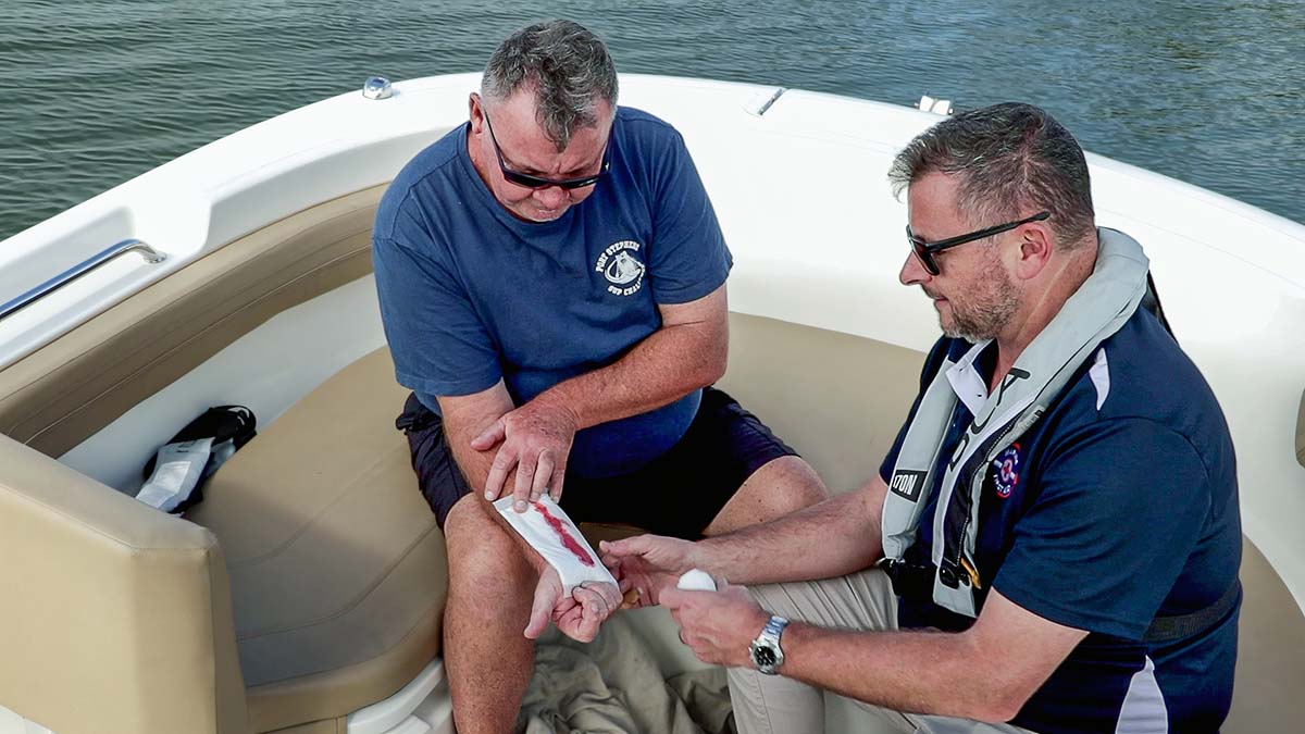 Marine First Aid responder on a boat treating casualty with cut to inner forearm