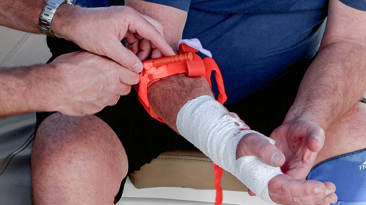Close up of marine first aid responder applying tourniquet to arm of casualty, bandage and bleeding visible on forearm