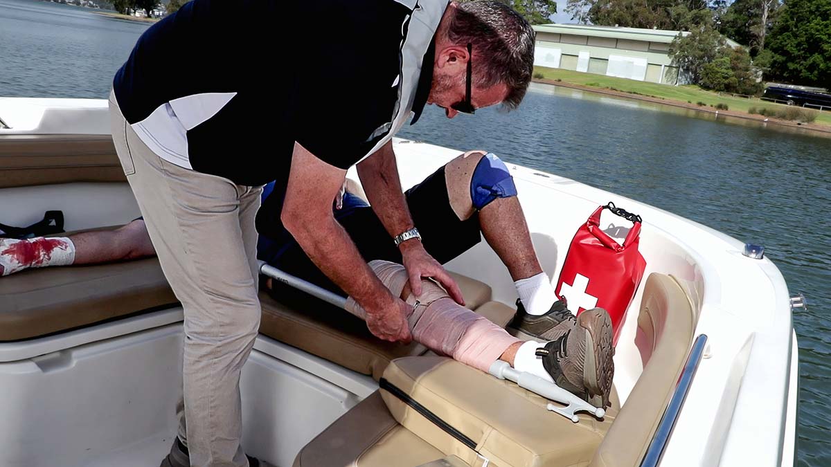 Marine First Aid responder using boat hook as makeshift splint for casualty on the bow seats of a boat